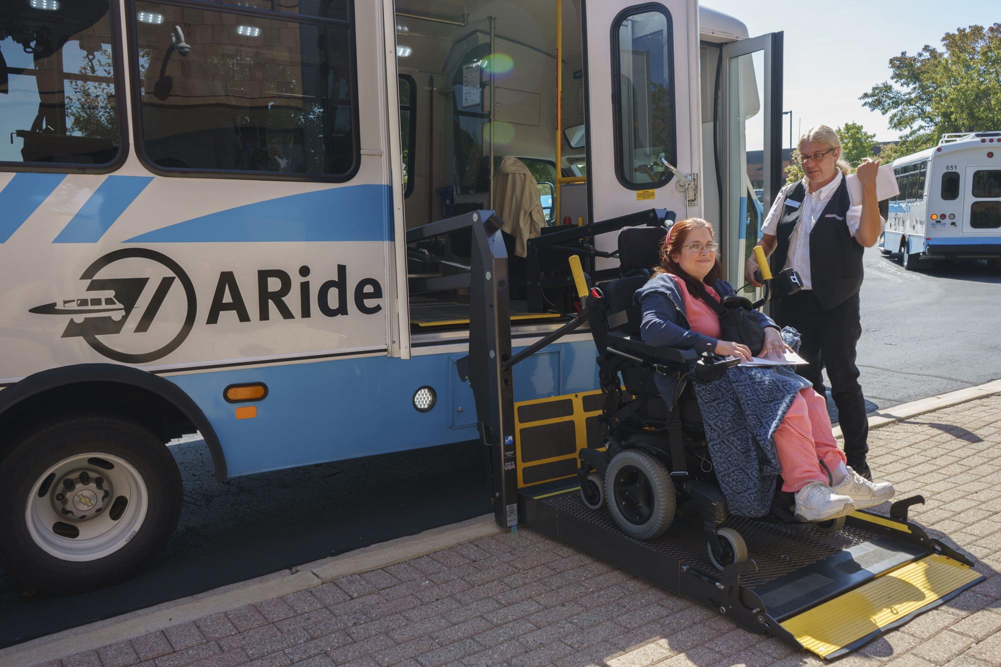 A woman has help boarding the A-Ride bus with her wheelchair.