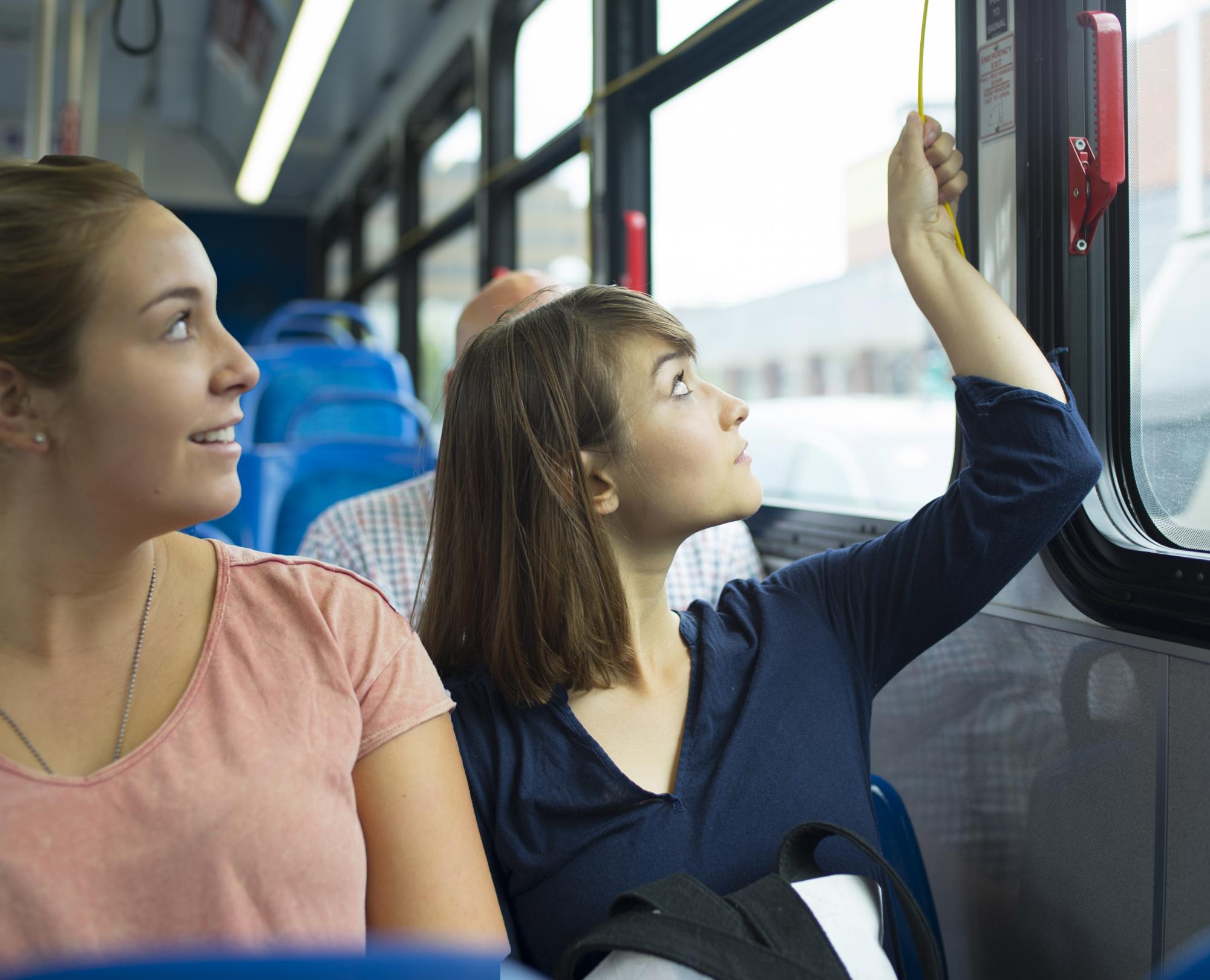 A woman pulls the cord to let the bus driver know she needs to get off the bus at the next stop.