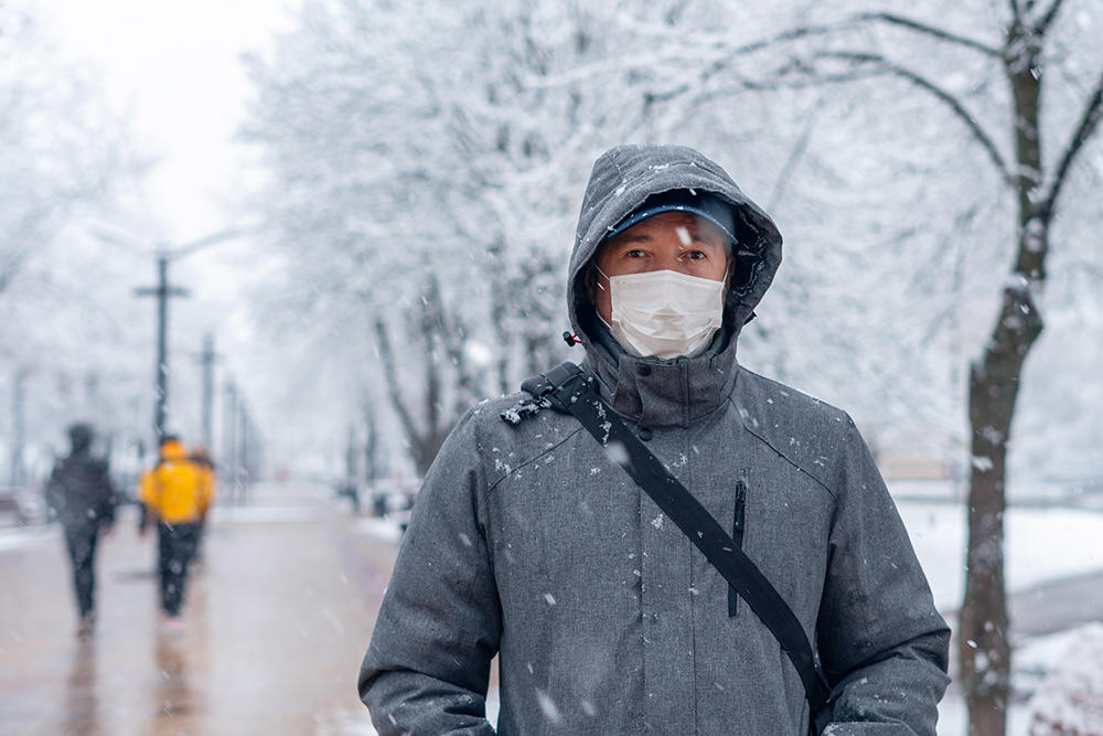 man wearing mask winter coat walking in snow