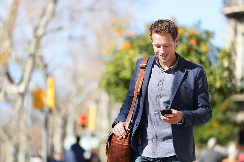 Man walking with messenger bag looking at phone