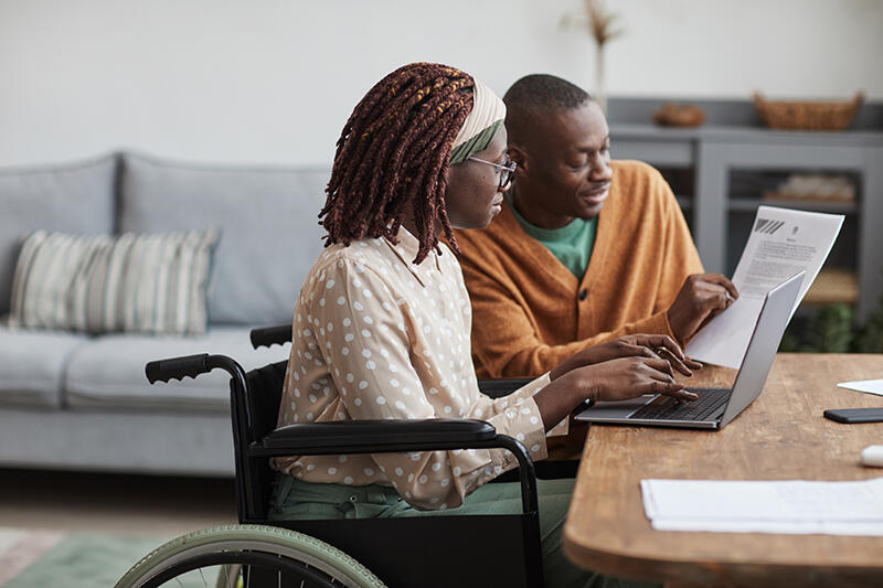 African American woman in wheelchair with man looking at computer