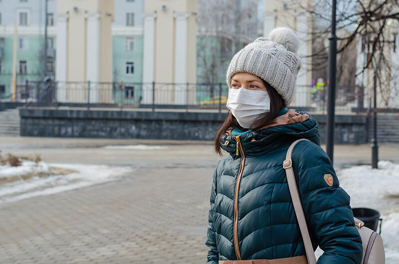 Woman in winter clothing wearing a mask on campus