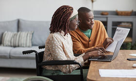 African American woman in wheelchair with man looking at computer