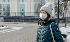 Woman in winter clothing wearing a mask on campus